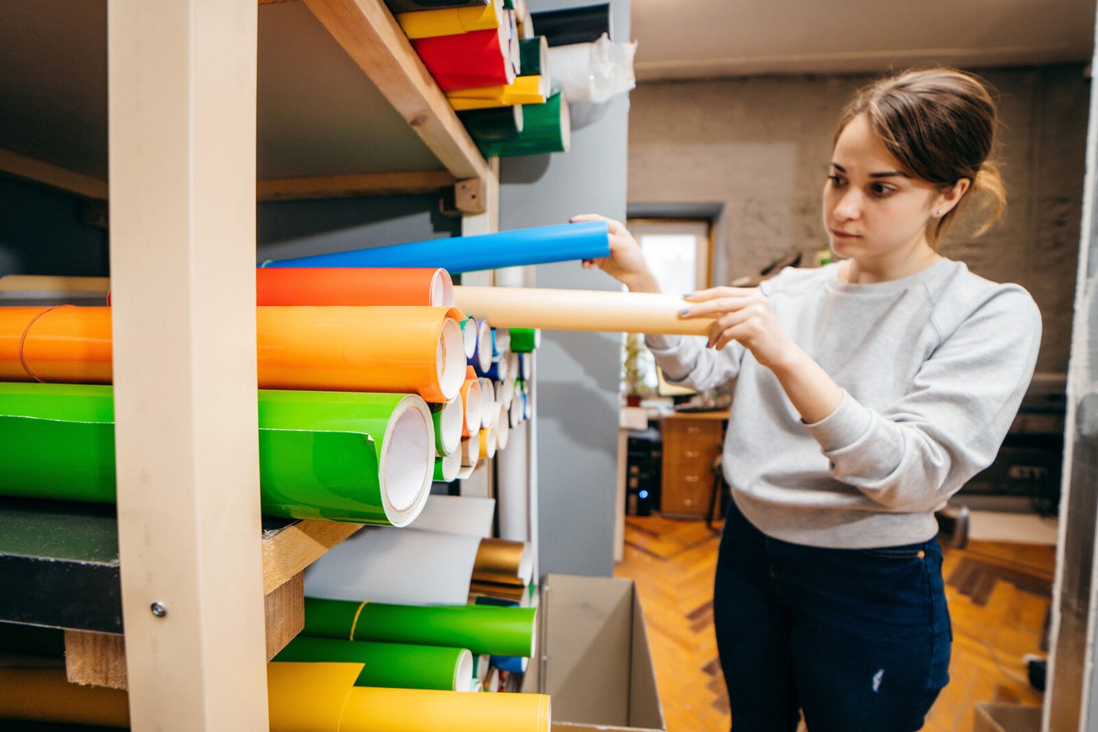 Woman chooses vinyl film of different colors in round tubes.