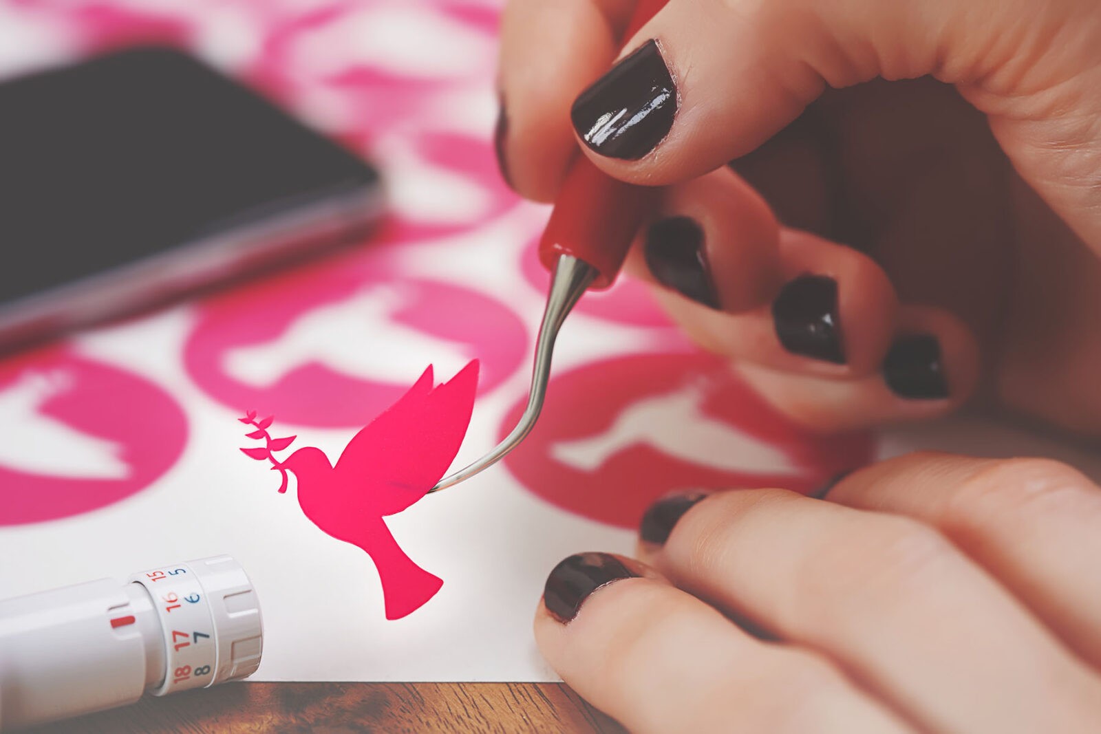 Hands use a hook weeding tool to life a vinyl dove design.